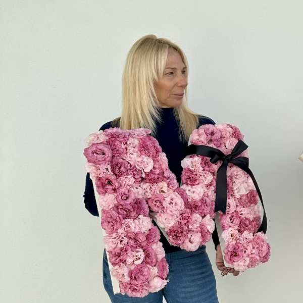 Woman holding two large pink floral letter arrangements