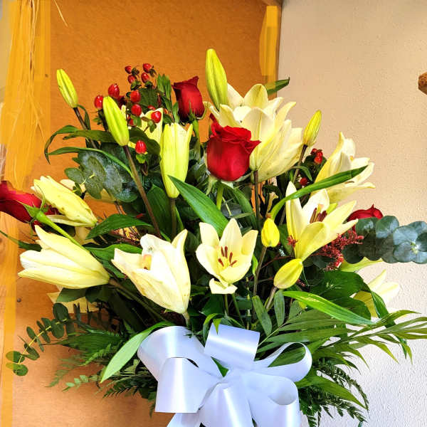 Tall bouquet of white lilies and red roses in a glass vase with a white ribbon