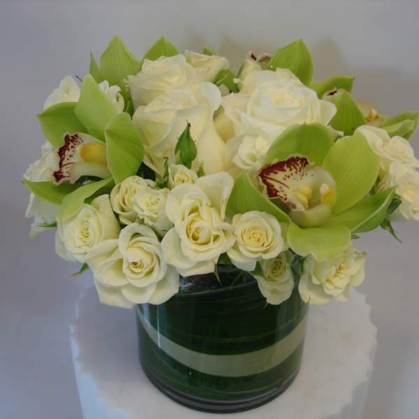 White roses and green orchids arranged in a glass vase