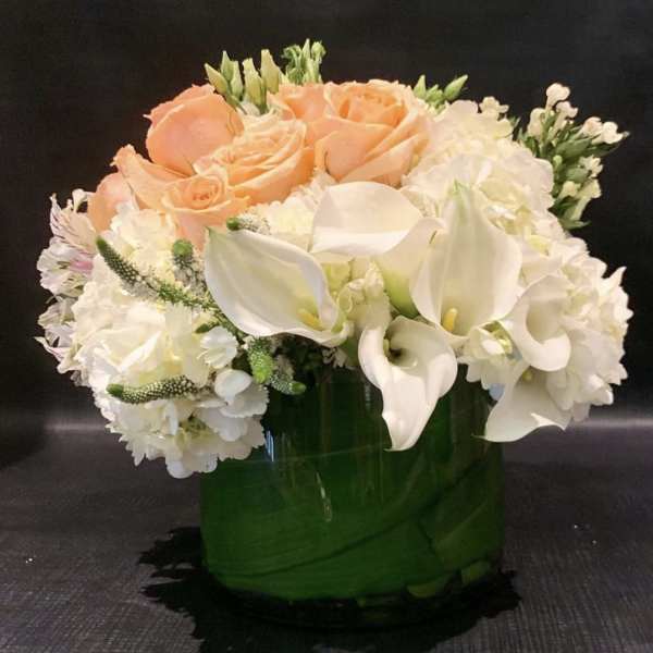 Peach roses and white calla lilies in a green glass vase