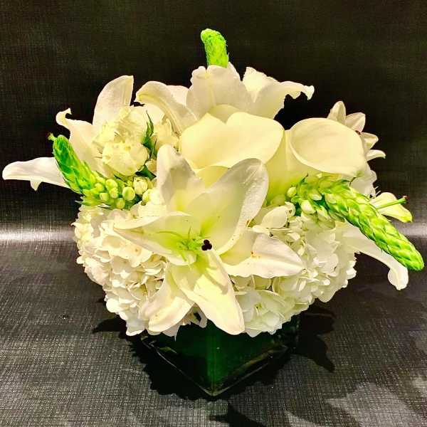 White lilies and hydrangeas arranged in a low vase with green accents