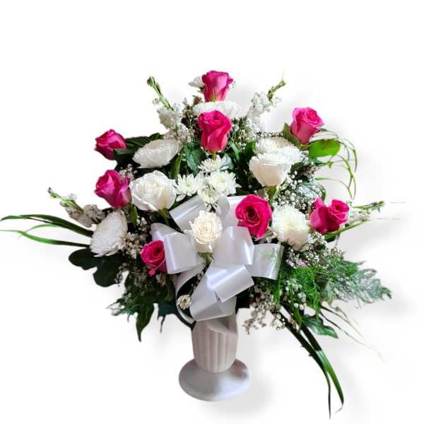 Pink and white rose arrangement in a white vase with a satin bow
