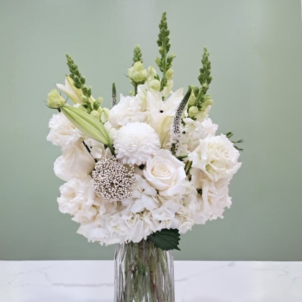 White floral arrangement in a clear glass vase with tall green spikes