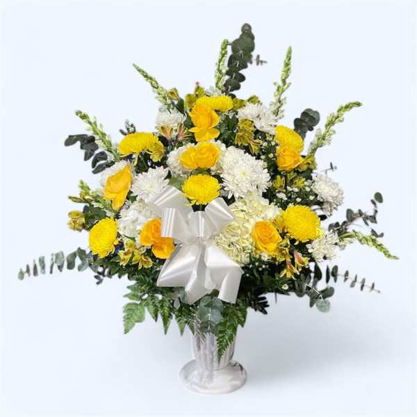 Yellow and white floral arrangement in a silver vase with a white bow