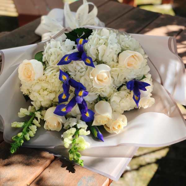 Bouquet of white flowers with cream roses and blue irises in pale wrapping