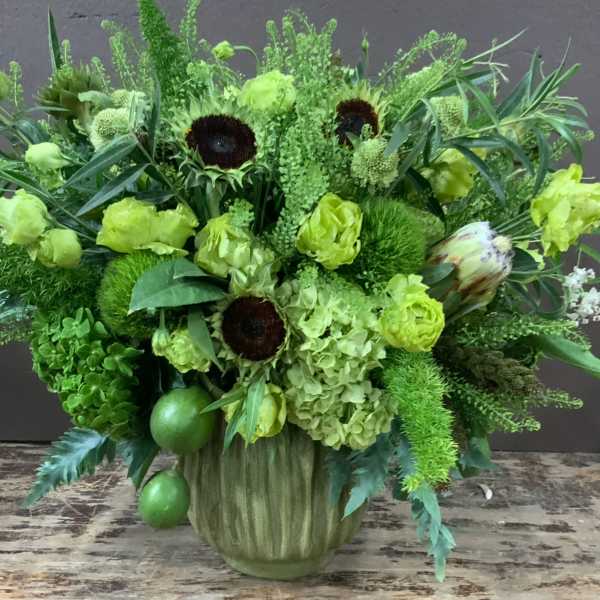 Green floral arrangement in a ribbed vase with sunflowers and hydrangeas