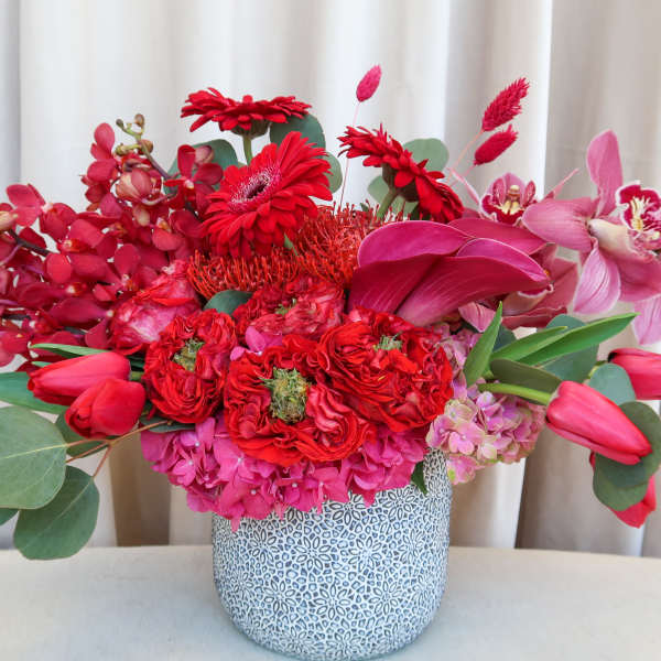 Red and pink floral arrangement in a patterned ceramic vase