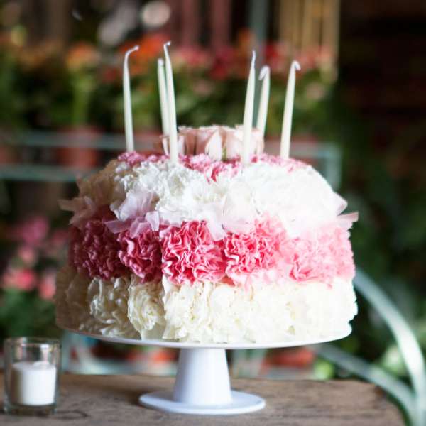 Pink and white floral cake with tall candles on a pedestal stand