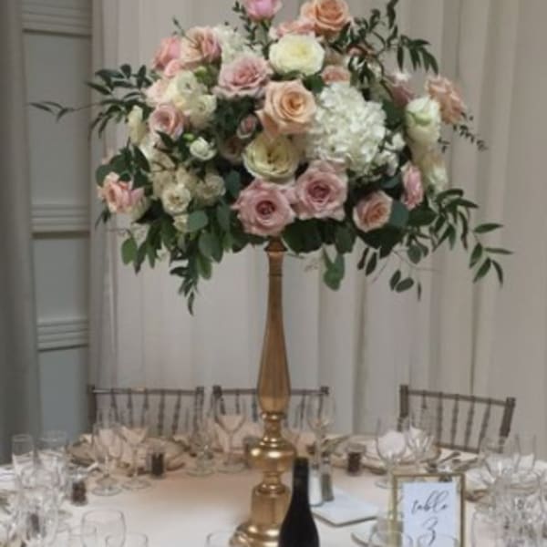 Tall floral centerpiece with pink and white roses on a gold stand