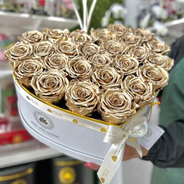 Heart-shaped white box filled with metallic gold roses and tied with a white logo ribbon