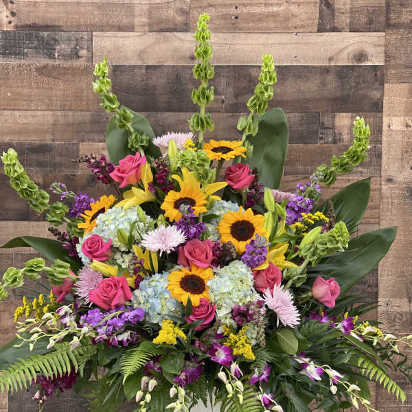 Large mixed bouquet with sunflowers, pink roses, lilies, and hydrangeas in a white vase