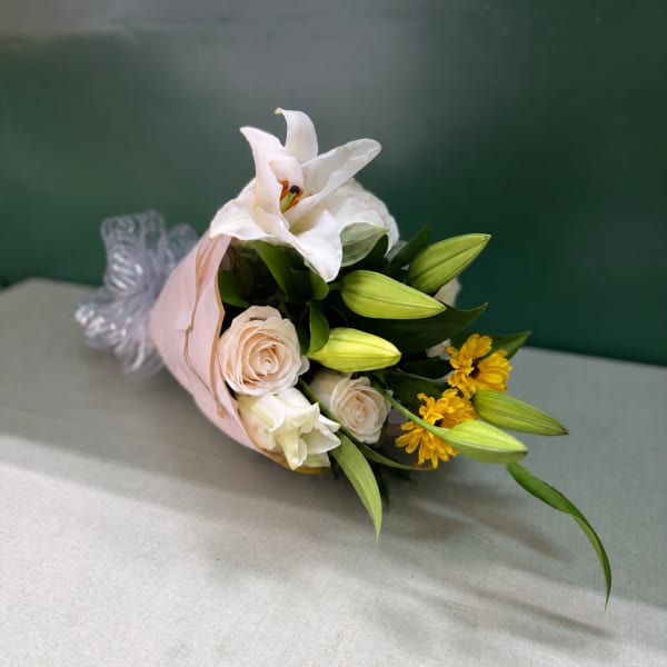 Bouquet of white lilies, pale roses, and yellow flowers wrapped in pink paper