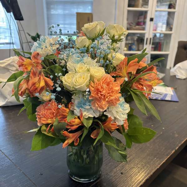 Bouquet of cream roses, orange alstroemeria, and blue filler in a glass vase
