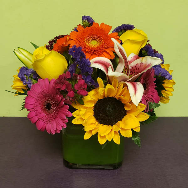 Colorful mixed bouquet in a green glass vase with sunflowers and roses