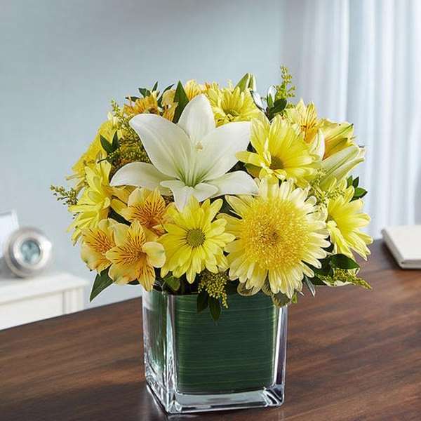 Yellow and white flower arrangement in a square glass vase