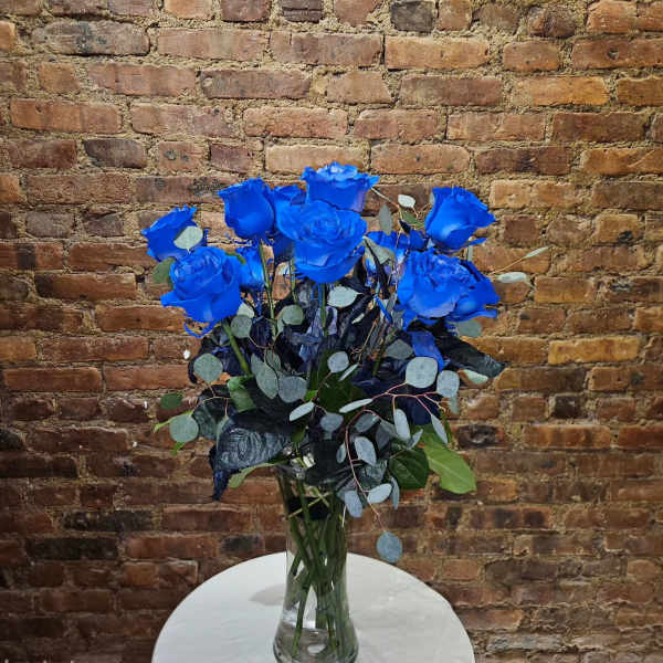 Blue roses arranged in a clear glass vase with mixed foliage