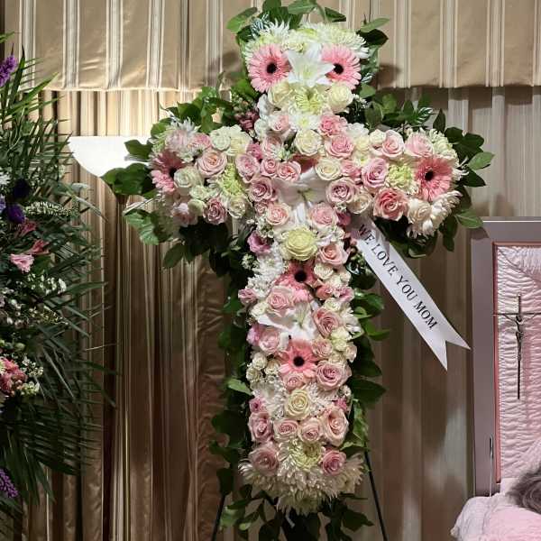 Large cross-shaped floral tribute with pink and white flowers on an easel