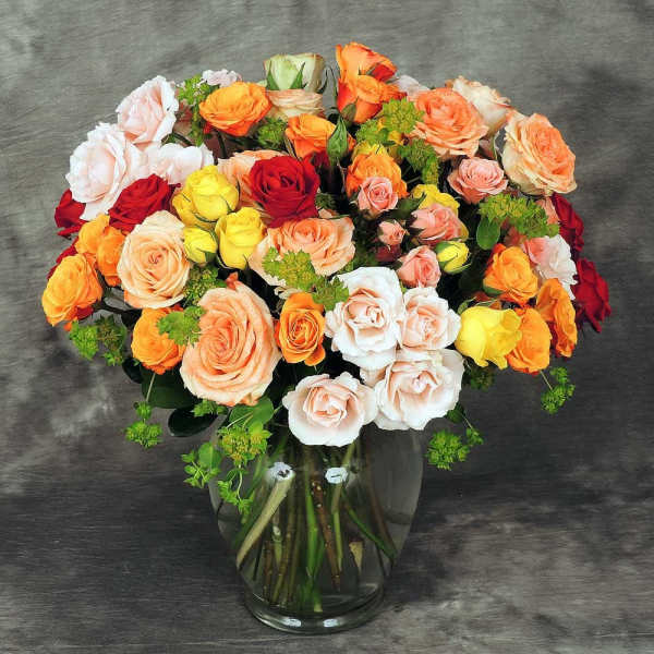 Mixed roses in orange, peach, red, yellow, and white in a glass vase.