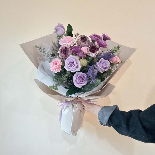 Hand-tied bouquet of lavender roses and pink flowers wrapped in paper