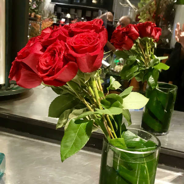 Red roses in a clear glass vase with green leaves