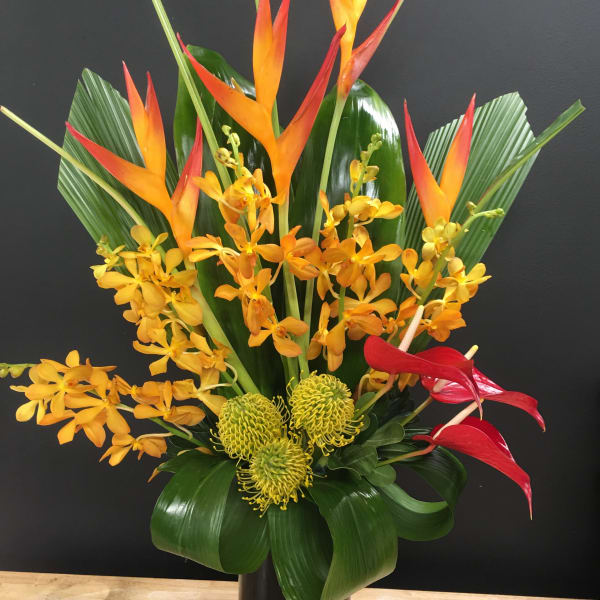 Tropical arrangement with orange heliconia, yellow orchids, and red anthuriums in a black vase