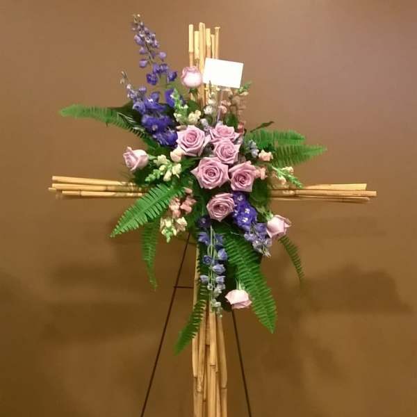 Standing floral cross with pink roses and purple flowers on a bamboo easel