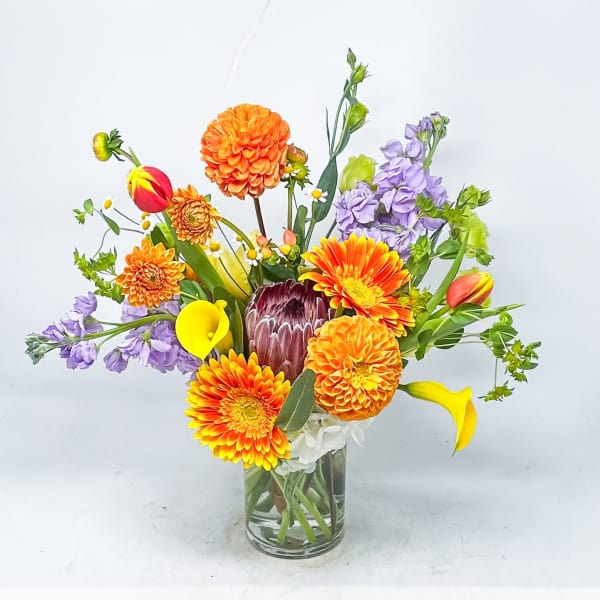 Colorful mixed bouquet in a clear glass vase with orange, purple, yellow, and white blooms