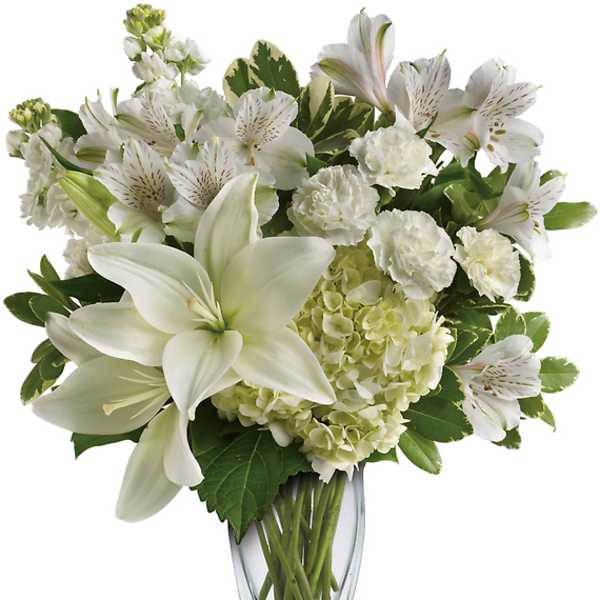 White lilies and mixed white flowers in a clear glass vase