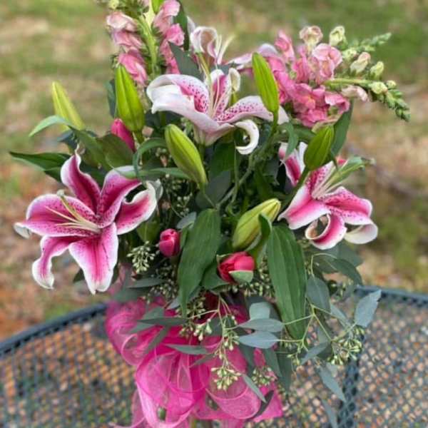 Pink lilies and snapdragons in a glass vase with a pink ribbon