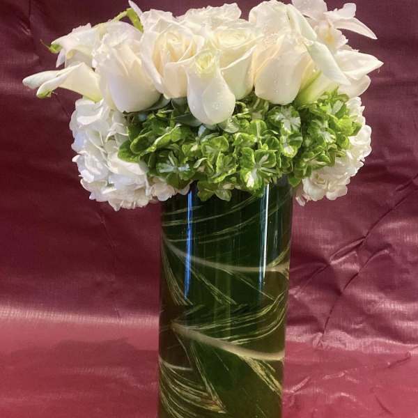 White roses and hydrangeas arranged in a tall glass vase
