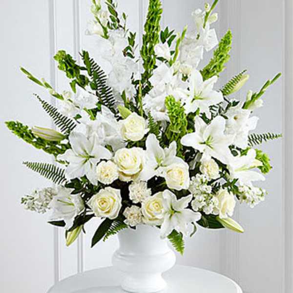Large white arrangement of lilies, roses, and carnations in a white pedestal vase