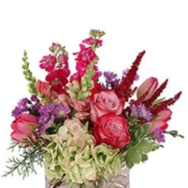 Mixed bouquet of pink, red, and purple flowers in a square glass vase
