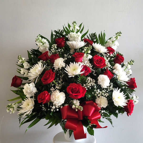 Red roses and white daisies in a white vase with a red ribbon