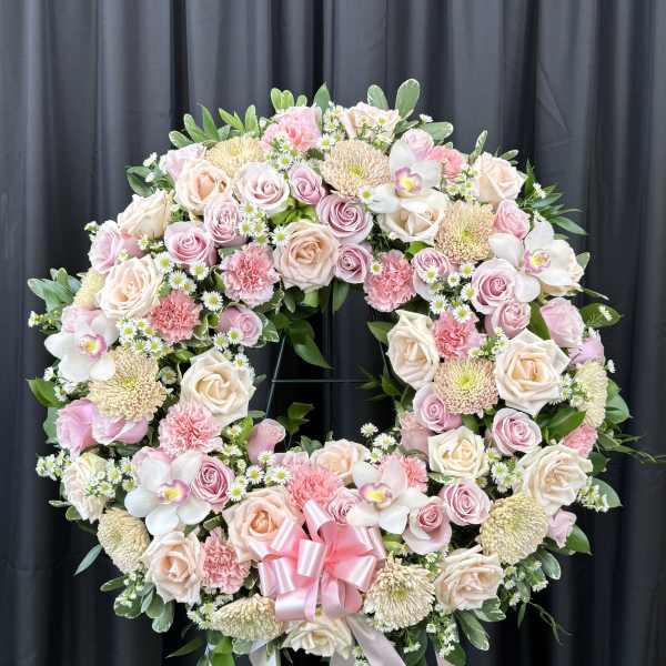 Large pink and cream floral wreath on a stand with a pink ribbon bow
