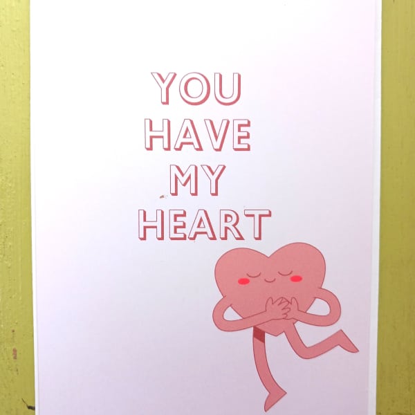 White greeting card with pink text 'You Have My Heart' and a smiling pink heart character hugging itself.