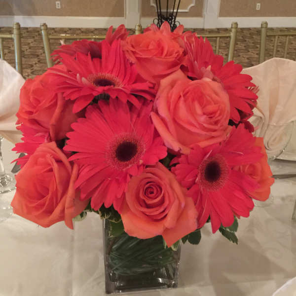 Pink and coral roses with hot pink gerbera daisies in a clear square vase