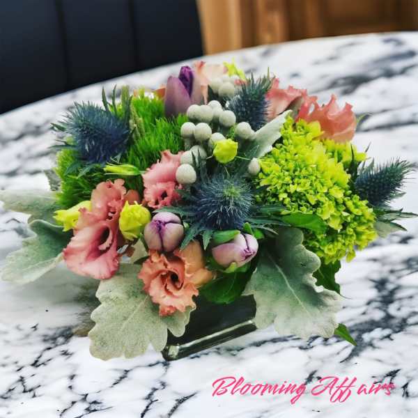 Compact mixed bouquet with pink, purple, and green blooms in a low glass vase