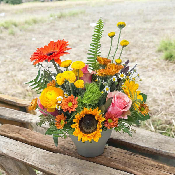 Colorful mixed flower arrangement in a gray vase with sunflowers and roses