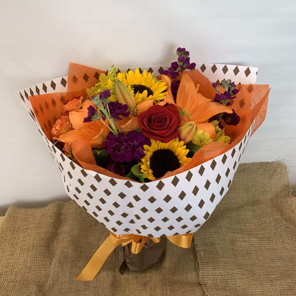 Bouquet of sunflowers, roses, lilies, and purple flowers wrapped in patterned paper