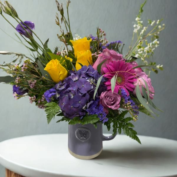 Mixed bouquet of purple, pink, and yellow flowers in a mug vase