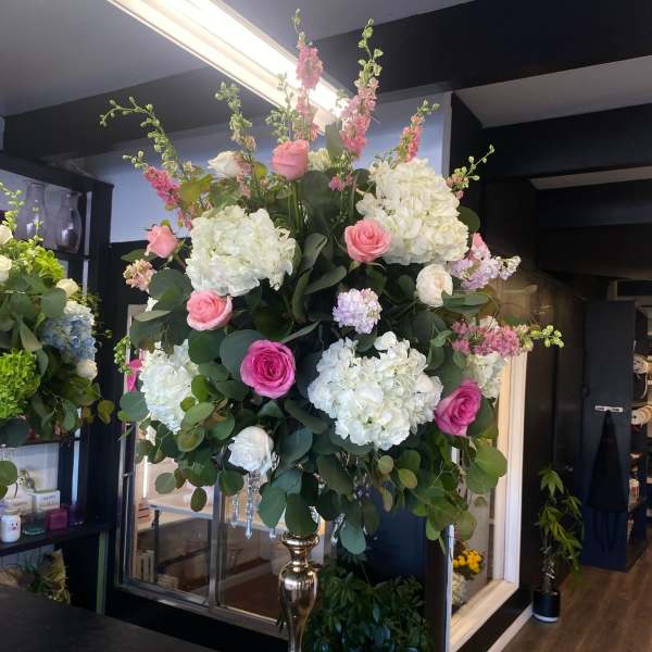Large pink and white floral arrangement in a tall gold vase