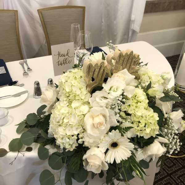 White floral centerpiece with roses and hydrangeas on a table