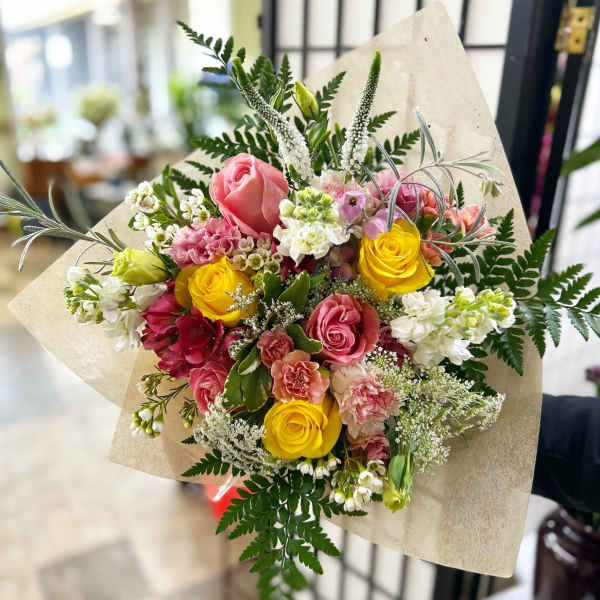 Bouquet of pink and yellow roses with mixed flowers wrapped in beige paper