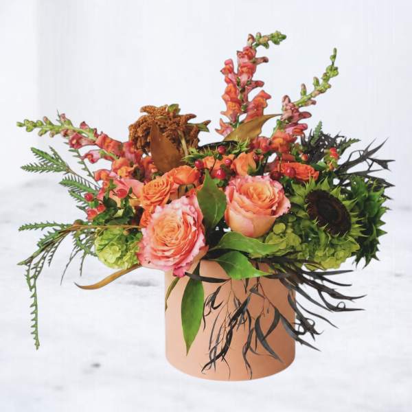 Peach roses and orange snapdragons in a round vase with mixed foliage