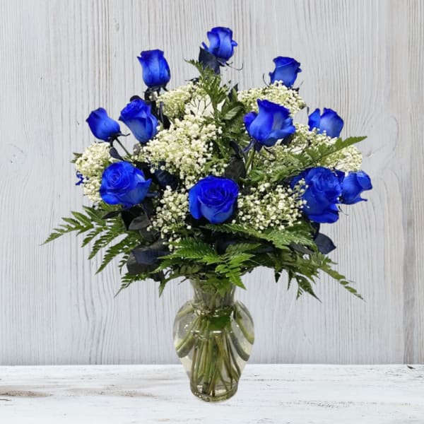 Arrangement of vivid blue roses with white filler flowers in a clear glass vase