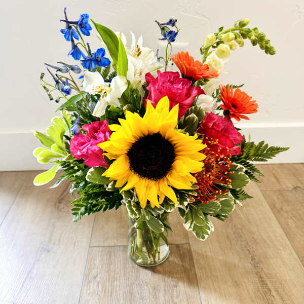 Colorful bouquet with a sunflower, gerbera daisies, and lilies in a glass vase