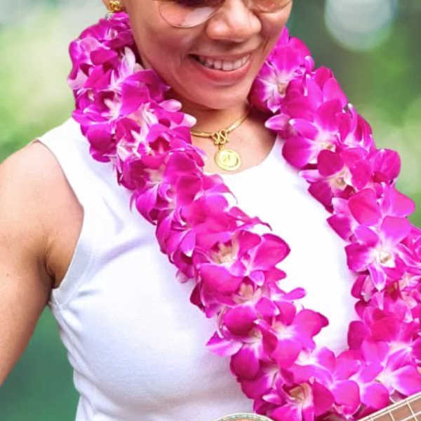 Woman wearing a bright pink orchid lei and holding a guitar