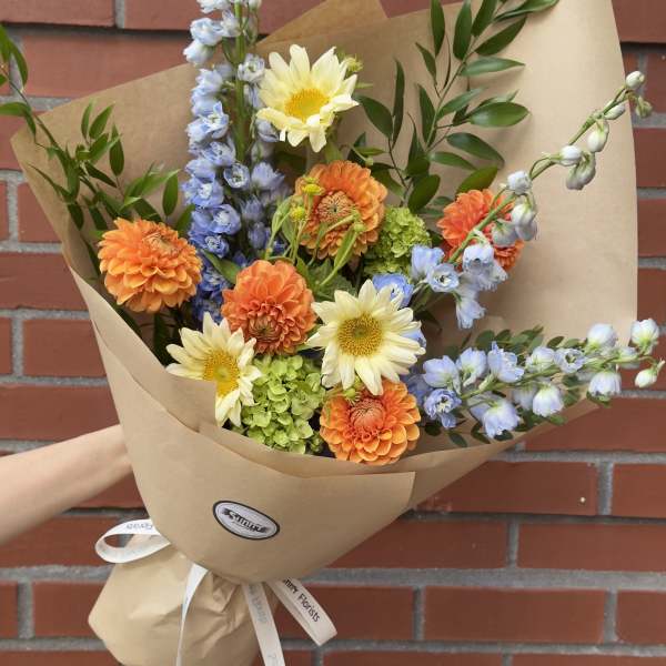 Bouquet of orange and pale yellow flowers wrapped in brown paper