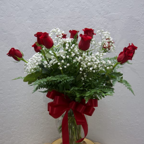 Red roses and white baby's breath in a glass vase with a red ribbon