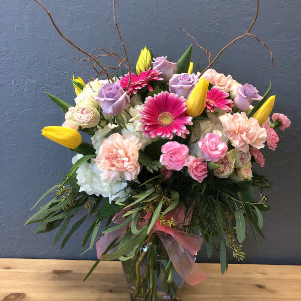 Mixed bouquet of pink, lavender, and yellow flowers in a glass vase